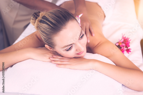 Young beautiful woman enjoying spa body massage at spa salon. Caucasian woman get happy, relax, calm on bed at spa salon. It traditional masseuse massaging on customers back, massage and spa concept