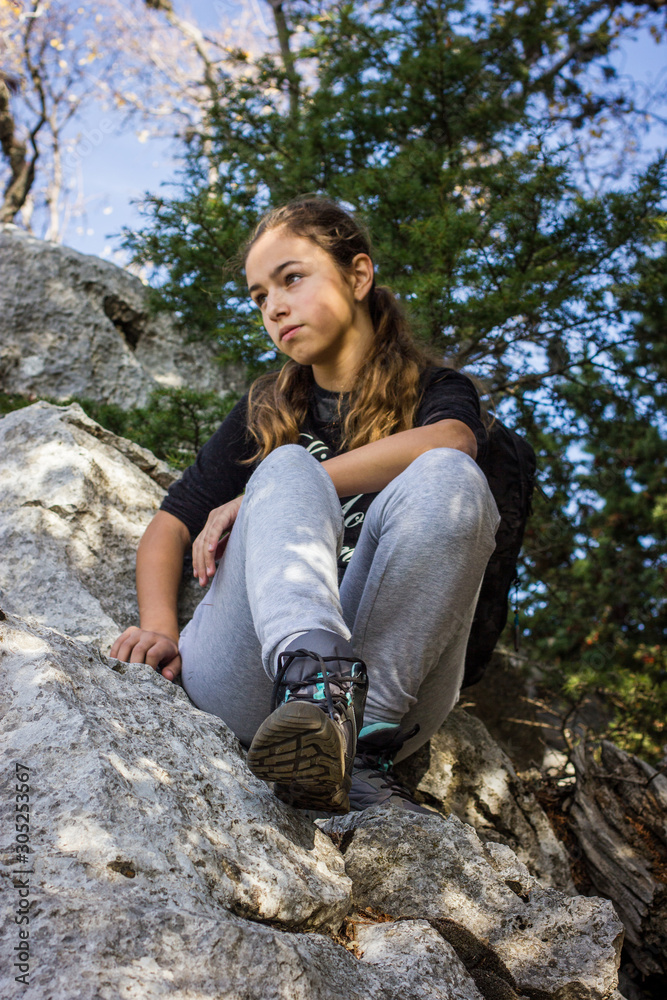 Obraz premium Young beautiful teenager girl sitting on a rock in a forest. Mountain climbing