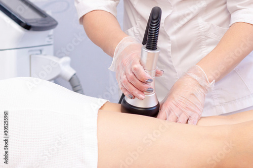 Cosmetologist reducing cellulite on the hips of a female patient, using ultrasound cavitation machine. Cropped shot of a woman getting rf lifting treatment on the back of her legs
