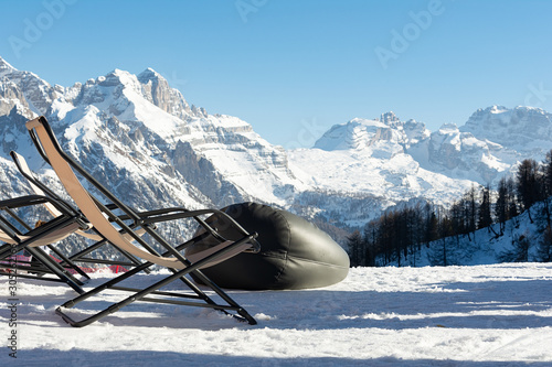 Empty deckchairs stand in the snow against the backdrop of snow-capped mountains. The concept of vacation, landscape. photo