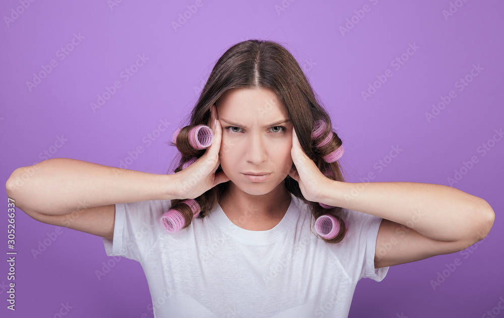 A girl in pink curlers on the background looks straight. A girl in pink curlers on the background looks straight.