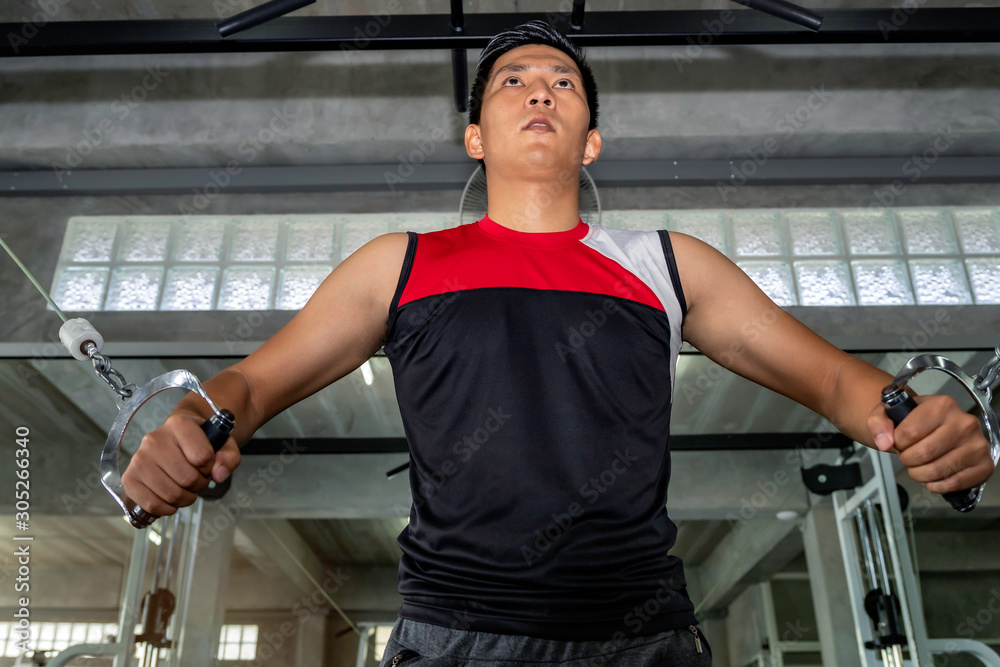 Athletic muscular handsome Asian man workout chest with cable in fitness gym.