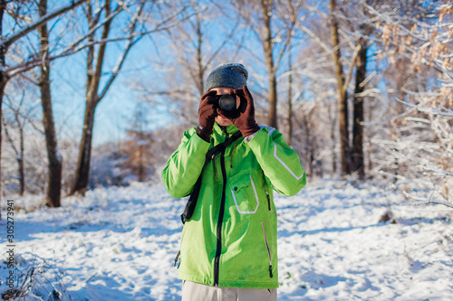 Young photographer takes pictures of winter forest using camera. Young man shooting photos outdoors