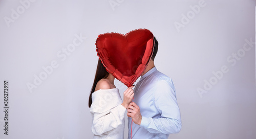 Loving couple kisses hiding behind a red ball in the shape of a heart.