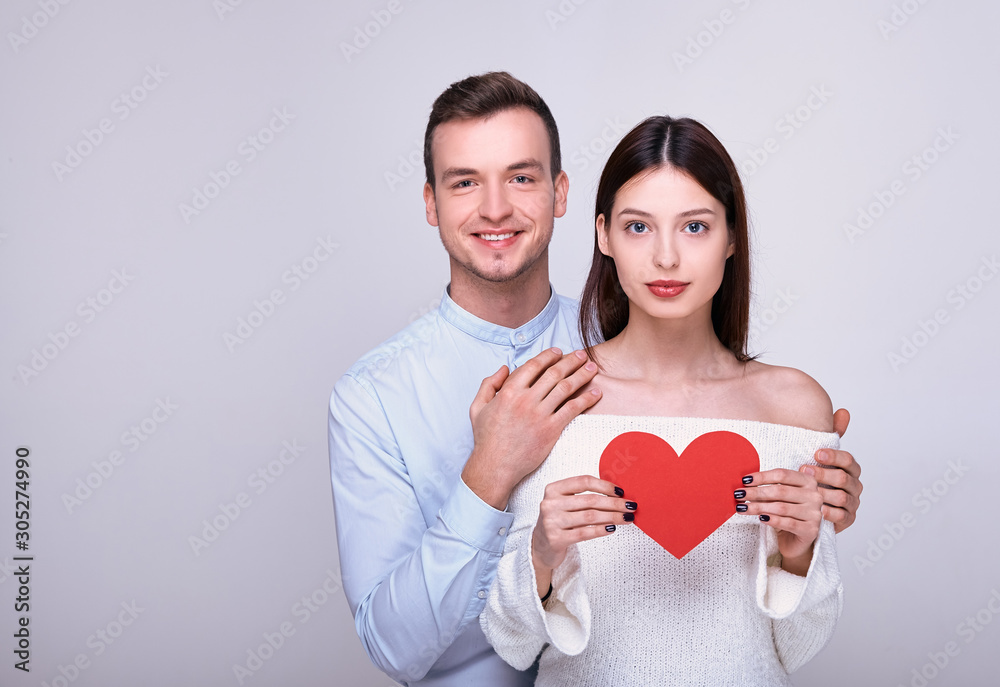 Nice smiling guy hugs beautiful girl who is holdingred cardboard heart