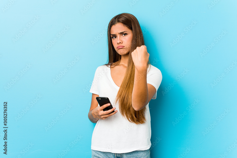Young caucasian woman holding a phone showing fist to camera, aggressive facial expression.