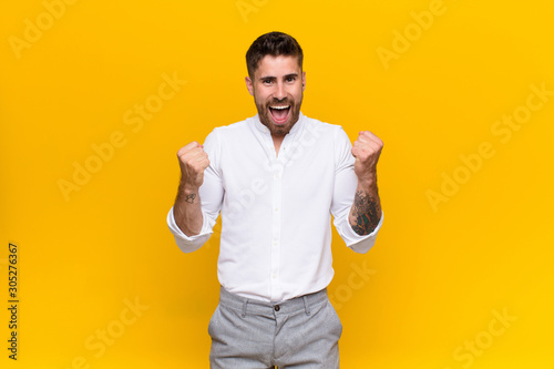 young handosme man feeling shocked, excited and happy, laughing and celebrating success, saying wow! against flat color wall photo