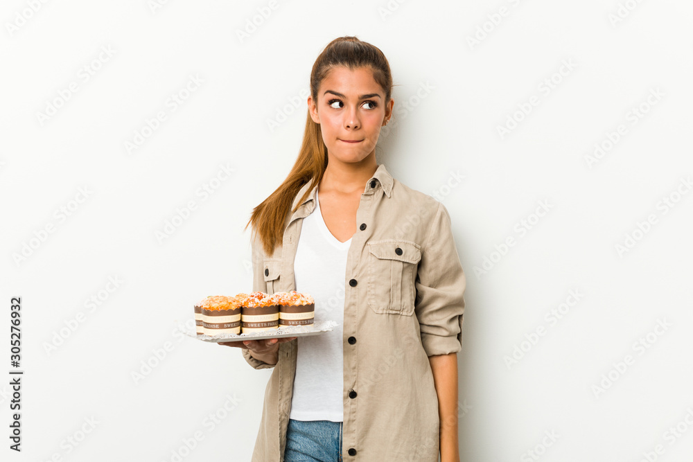 Young caucasian woman holding sweet cakes confused, feels doubtful and unsure. Young caucasian woman holding sweet cakes confused, feels doubtful and unsure.
