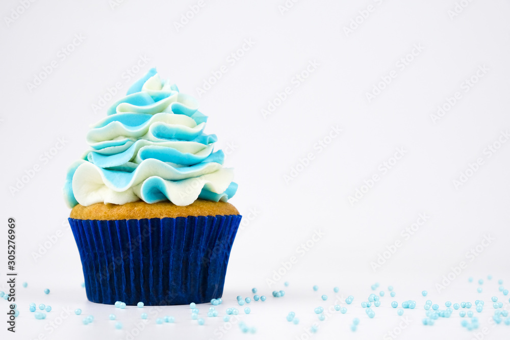 Cupcake on birthday with blue and white cream on white background, decorated with sprinkles.