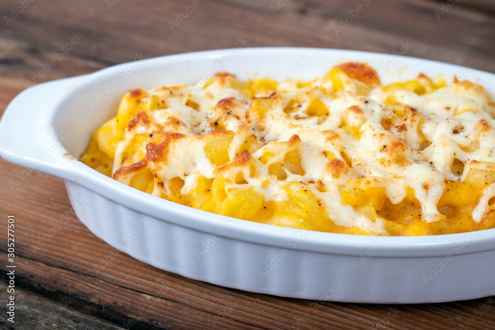 Butternut squash mac and cheese dish closeup on a rustic table and grated cheese on top Butternut squash mac and cheese dish closeup on a rustic table and grated cheese on top