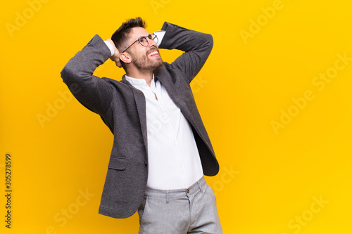 young handosme man smiling and feeling relaxed, satisfied and carefree, laughing positively and chilling against flat color wall photo