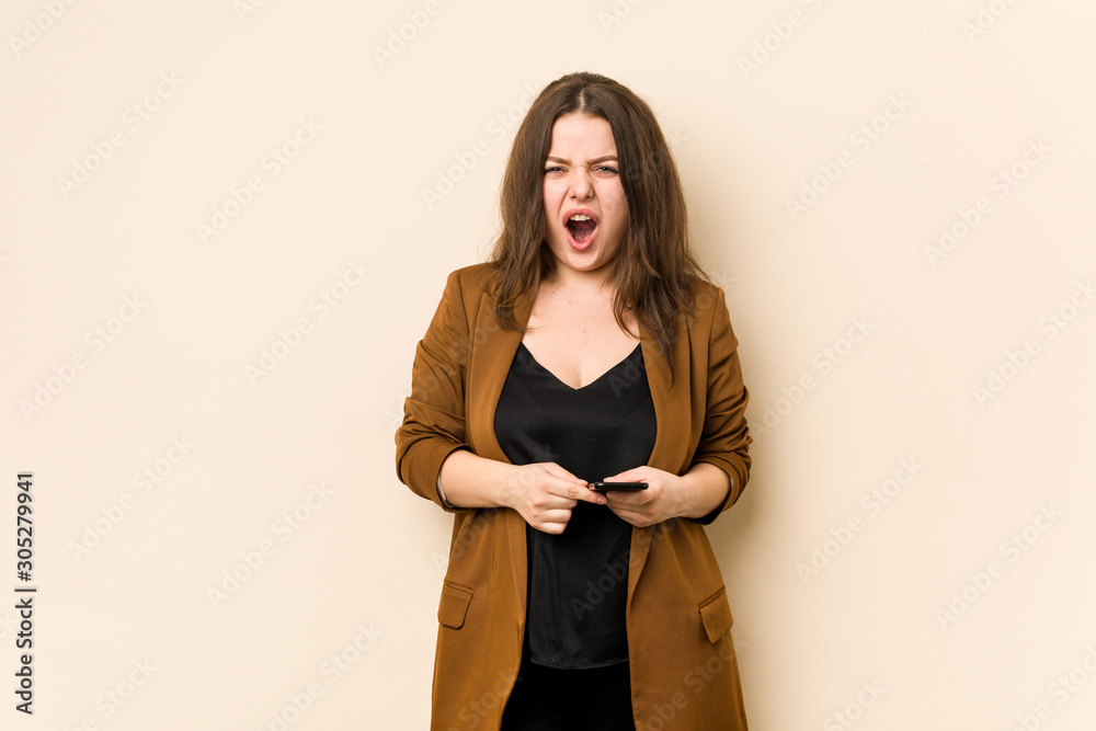 Young curvy woman holding a phone screaming very angry and aggressive. Young curvy woman holding a phone screaming very angry and aggressive.
