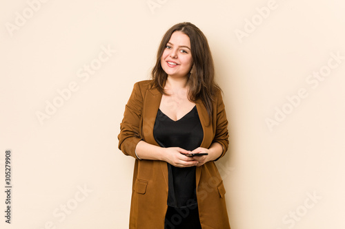 Young curvy woman holding a phone happy, smiling and cheerful. © Asier