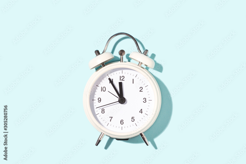 White alarm clock on blue background. Minimal styled, top view. White alarm clock on blue background. Minimal styled, top view.