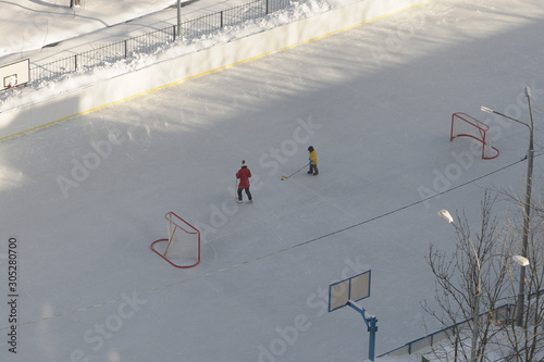 mom and son play hockey on an empty ice rink, top view