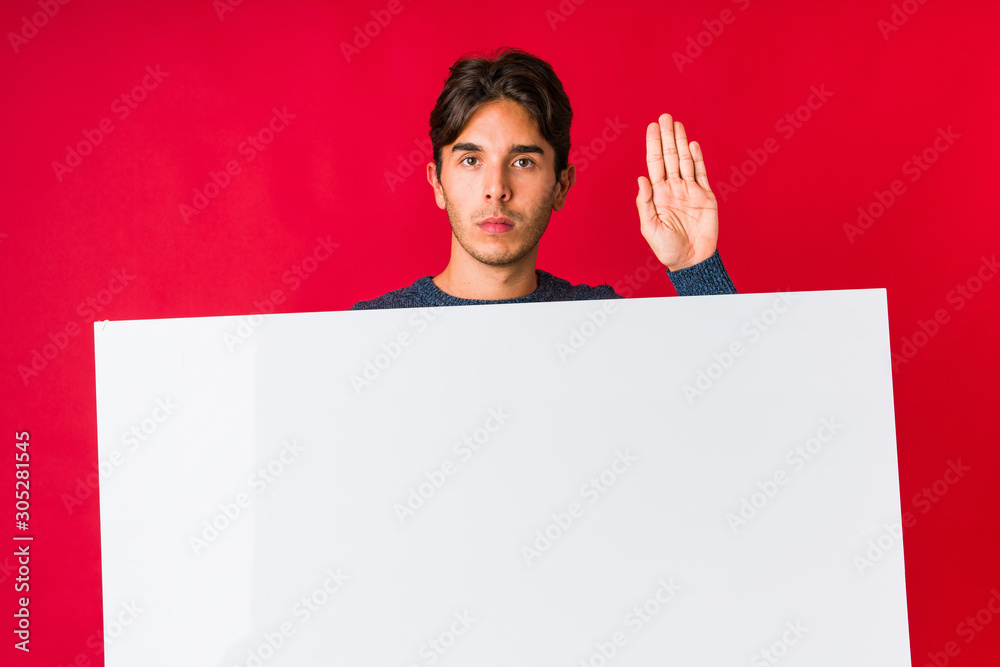 Young man holding a placard standing with outstretched hand showing stop sign, preventing you. Young man holding a placard standing with outstretched hand showing stop sign, preventing you.