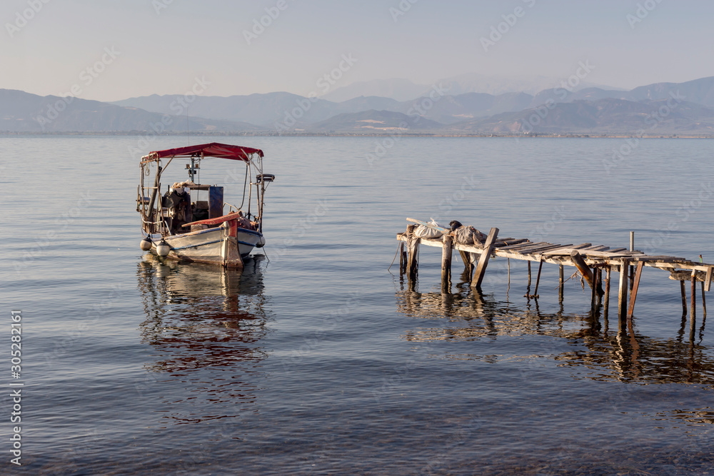 The fishing boat is moored near the shore and wooden, old pier close-up (Greece)