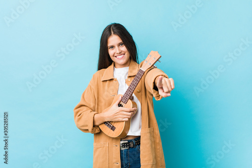 Canvas Print Young caucasian woman holding a ukelele cheerful smiles pointing to front