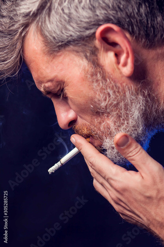 A portrait of the man smokes cigarette on black background. Nicotine addiction concept
