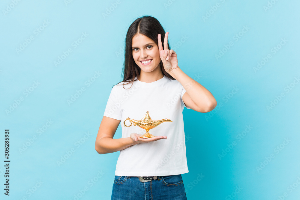 Young caucasian woman holding a magic lamp showing victory sign and smiling broadly. Young caucasian woman holding a magic lamp showing victory sign and smiling broadly.