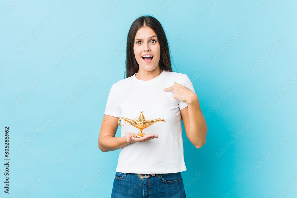 Young caucasian woman holding a magic lamp surprised pointing at himself, smiling broadly. Young caucasian woman holding a magic lamp surprised pointing at himself, smiling broadly.