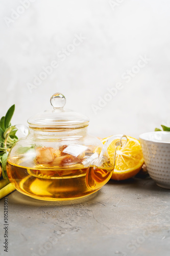 Making healthy antioxidant and anti-inflammatory ginger tea with fresh ginger, lemongrass, sage, honey and lemon on dark background with copy space.