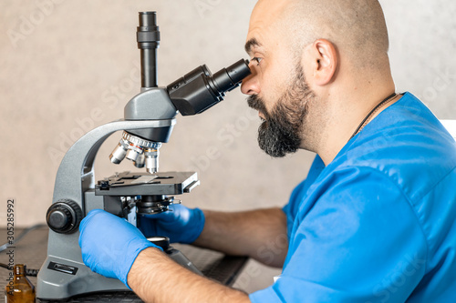 Male laboratory assistant examining biomaterial samples in a microscope