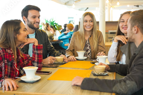 Group of people drinking cappuccino in a bar-  Friends hanging out with each other and talking- Smilie boys ang girls having conversations sitting around the coffee table- Lifestyle concept