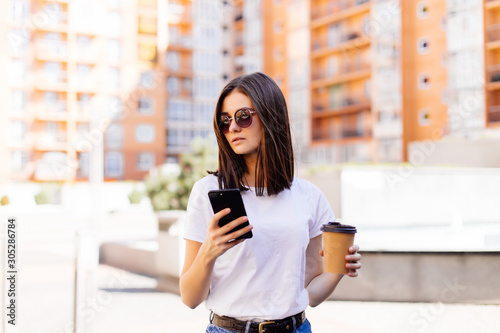 Beautiful young woman using her smart phone with smile while walking outdoors