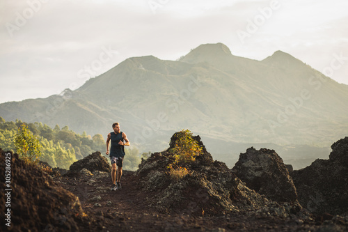 Young athlete man trail running in mountains in the morning. Amazing volcanic landscape of Bali mount Batur on background. Healthy lifestyle concept.