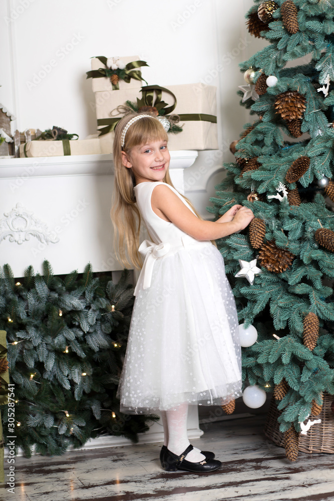 Cute little girl with long hair decorating christmas tree. Young kid in light bedroom with winter decoration. Happy family at home. Christmas New Year december time for celebration concept Cute little girl with long hair decorating christmas tree. Young kid in light bedroom with winter decoration. Happy family at home. Christmas New Year december time for celebration concept