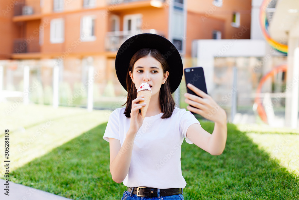 Portrait of young woman eating ice cream and taking selfie photo on camera in summer street. Portrait of young woman eating ice cream and taking selfie photo on camera in summer street.