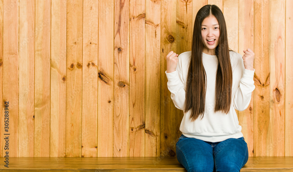 Young chinese woman sitting on a wooden place cheering carefree and excited. Victory concept. Young chinese woman sitting on a wooden place cheering carefree and excited. Victory concept.
