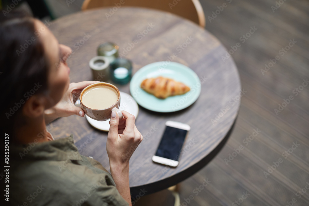 High angle view of young woman holding cup of fresh coffee latte over wooden table in french cafe, copy space