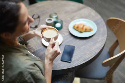 High angle view of smiling young woman holding cup of fresh coffee latte over wooden table in french cafe, copy space