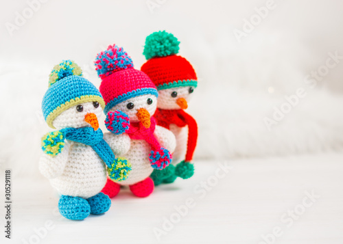 Three Little cute crocheted snowmans in a multicolor hats and scarfs on a white wooden background