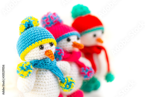 Three Little cute crocheted snowmans in a multicolor hats and scarfs on a white background.