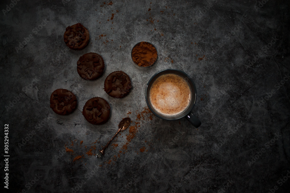 cocoa drink in blue mug with chocolate on dark textured background with chocolate muffins and vintage spoon and cocoa powder.