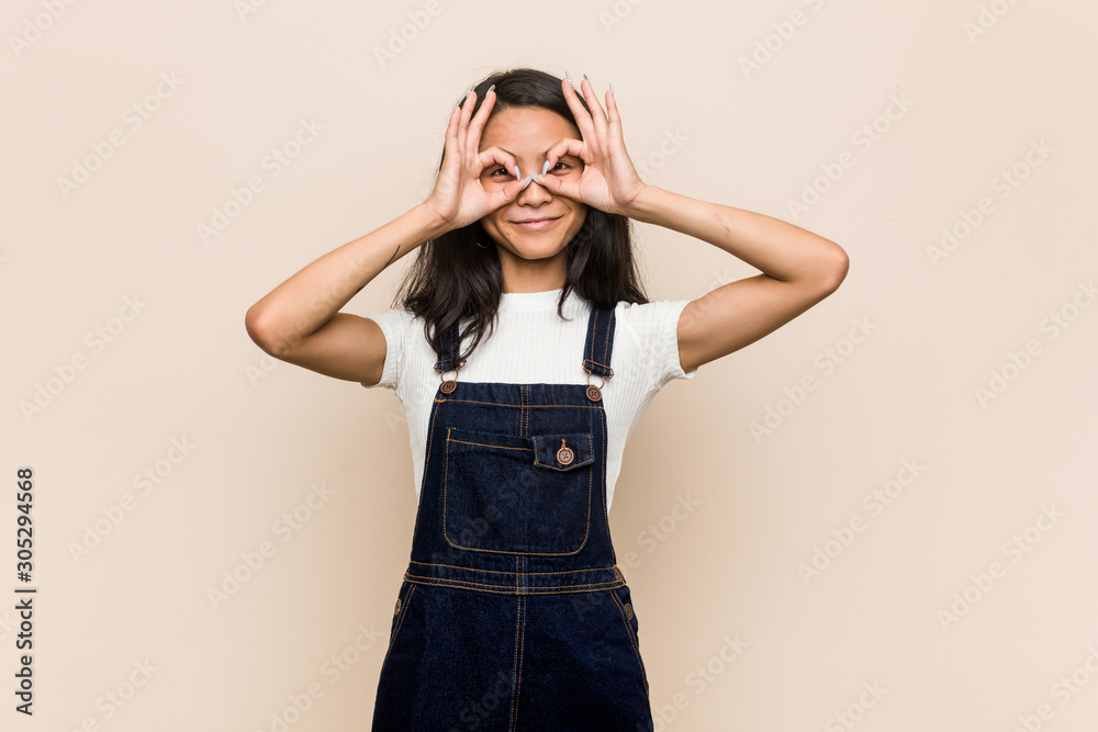 Young cute chinese teenager Young blonde woman wearing a coat against a pink background showing okay sign over eyes