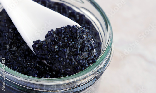 Black caviar closeup in open glass jar with white porcelain spoon