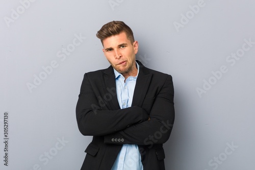 Young handsome caucasian man frowning face in displeasure, keeps arms folded.