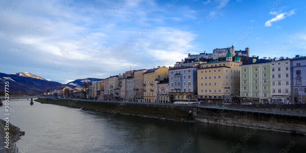 Salzburg riverfront shops with river Salzach and castle Hohensalzburg in sunny daylight.