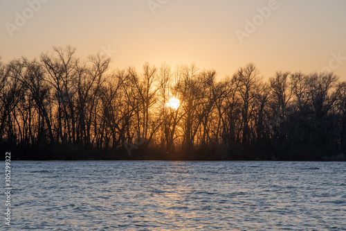 Landscape. Sunset behind the trees on the river. Late fall.