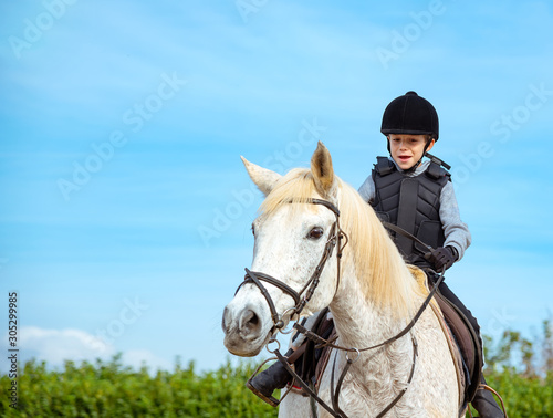 Kid riding white horse during horseback lessons, copy space.