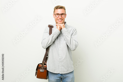 Young caucasian business man keeps hands under chin, is looking happily aside.