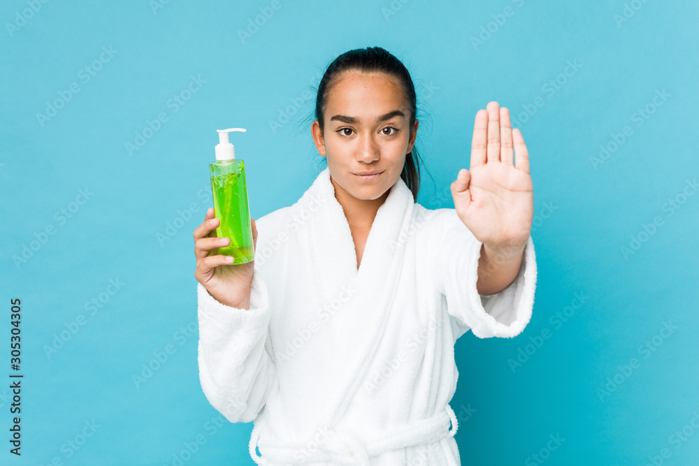 Young mixed race indian holding an aloe vera bottle standing with outstretched hand showing stop sign, preventing you. Young mixed race indian holding an aloe vera bottle standing with outstretched hand showing stop sign, preventing you.