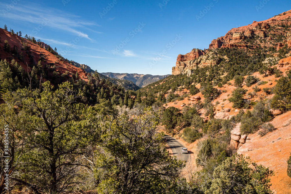 Silver SUV traveling on a road trip through a winding canyon beneath red rock cliffs and towers.