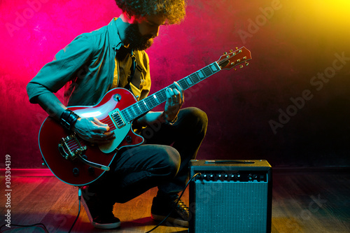 Portrait of hipster man with curly hair with red guitar in neon lights. Rock musician is playing electrical guitar. photo