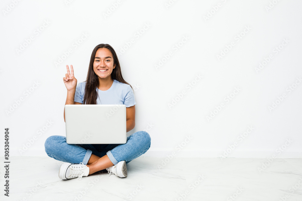 Young mixed race indian woman sitting working on laptop showing victory sign and smiling broadly. Young mixed race indian woman sitting working on laptop showing victory sign and smiling broadly.
