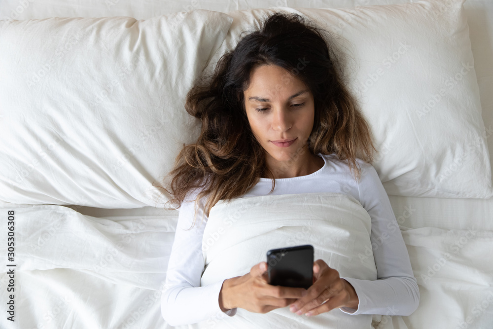 Above view 30s woman awakened checking social network messages